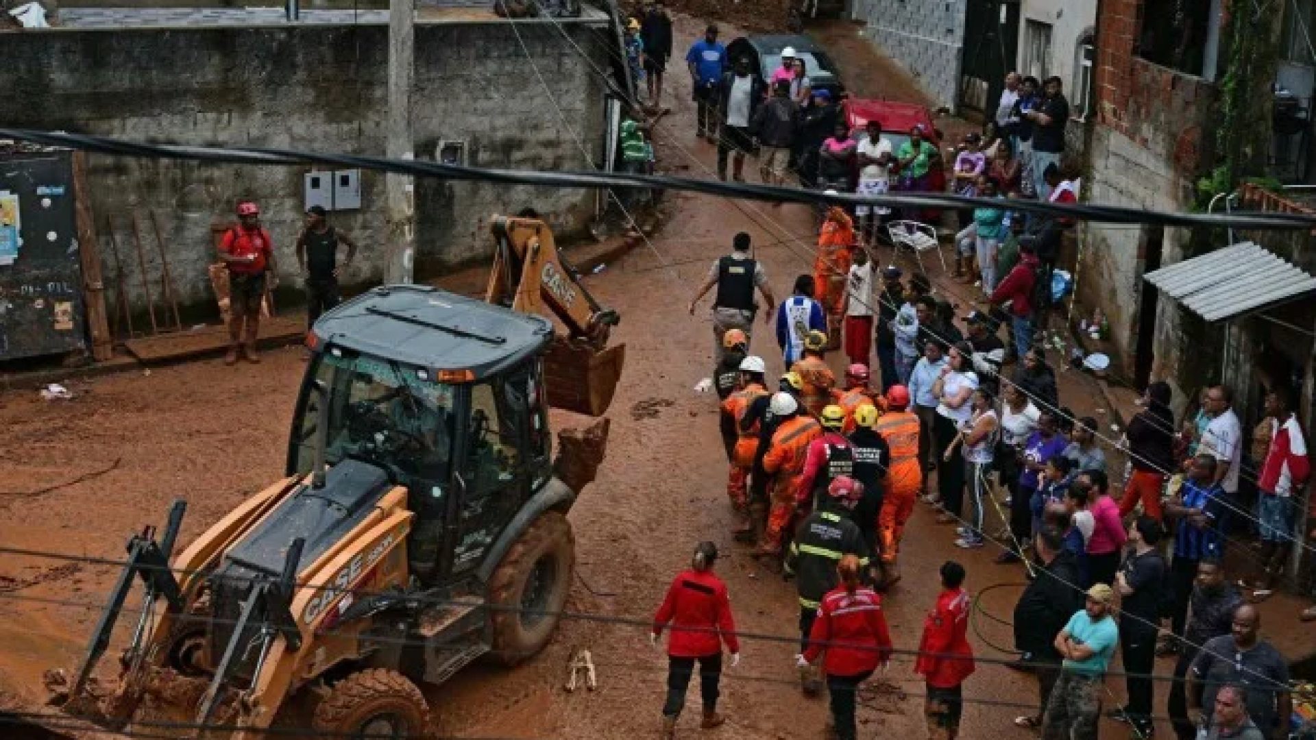 Equipes de resgate carregam um cadáver recuperado dos escombros, passando por uma retroescavadeira, após um deslizamento de terra causado por fortes chuvas no bairro Parque Jardim Burnier, em Juiz de Fora, Minas Gerais, Brasil, em 24 de fevereiro de 2026       -  (crédito: PABLO PORCIUNCULA / AFP)