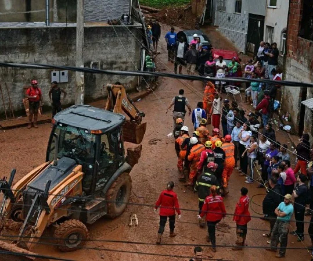 Equipes de resgate carregam um cadáver recuperado dos escombros, passando por uma retroescavadeira, após um deslizamento de terra causado por fortes chuvas no bairro Parque Jardim Burnier, em Juiz de Fora, Minas Gerais, Brasil, em 24 de fevereiro de 2026       -  (crédito: PABLO PORCIUNCULA / AFP)