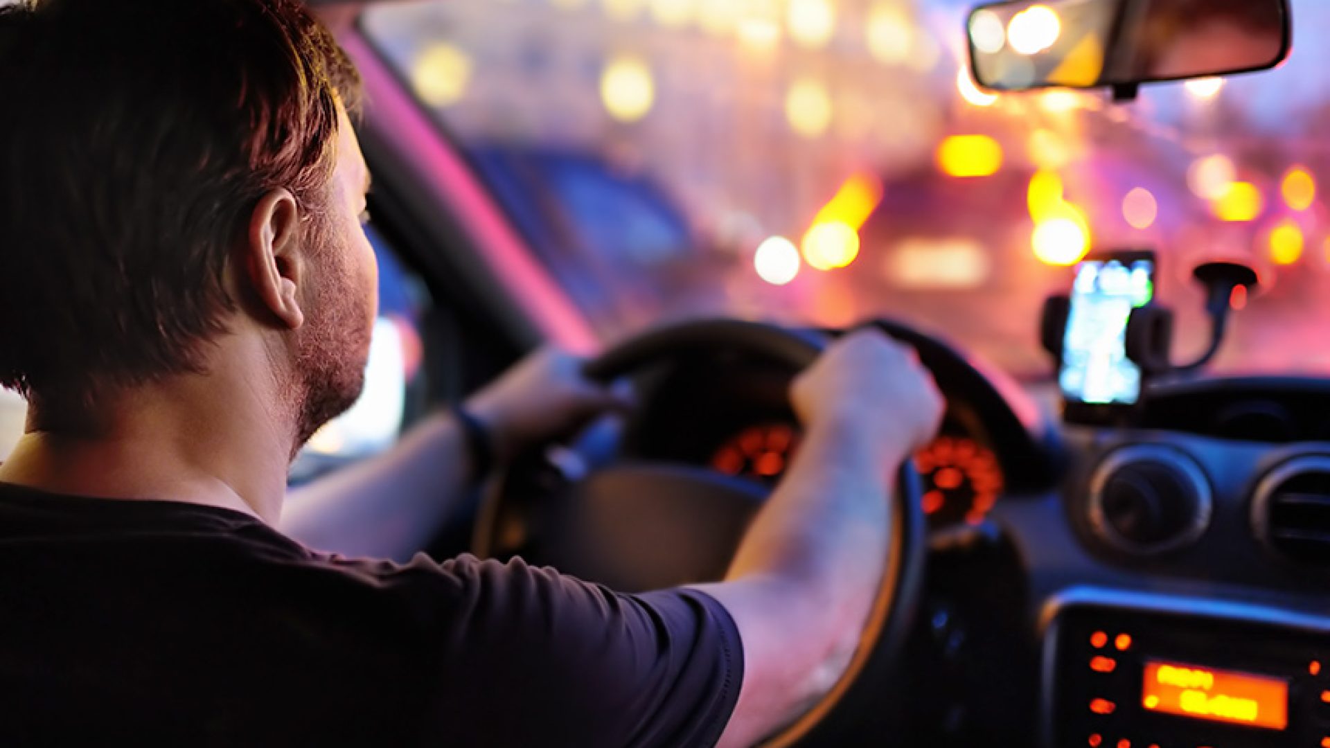 Motorista masculino dirige um carro durante o engarrafamento da noite. Vista interior.