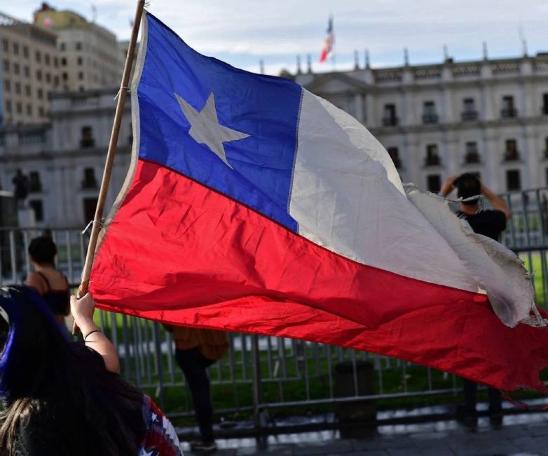 85292683_A-demonstrator-displays-a-Chilean-flag-as-she-walks-past-La-Moneda-Presidential-Palace.jpg