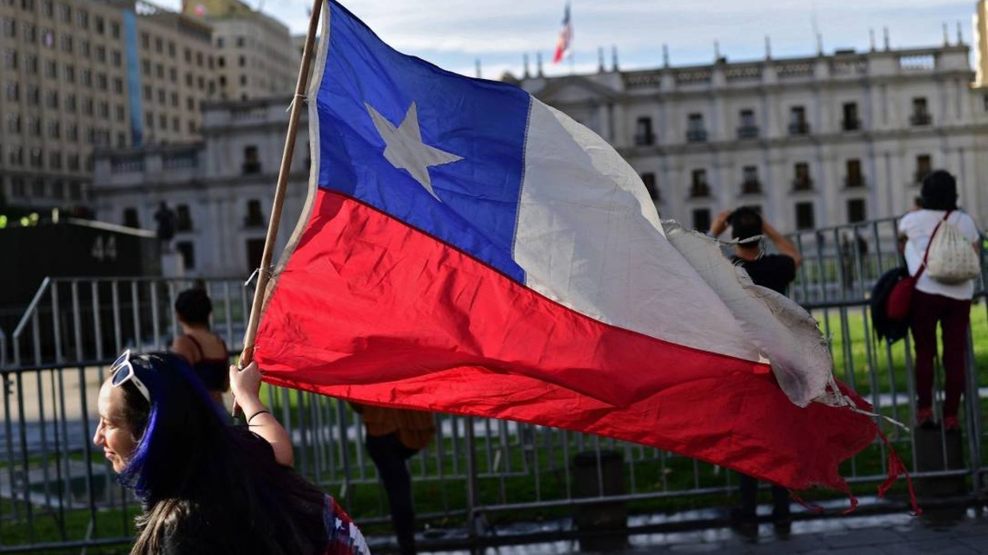 85292683_A-demonstrator-displays-a-Chilean-flag-as-she-walks-past-La-Moneda-Presidential-Palace.jpg