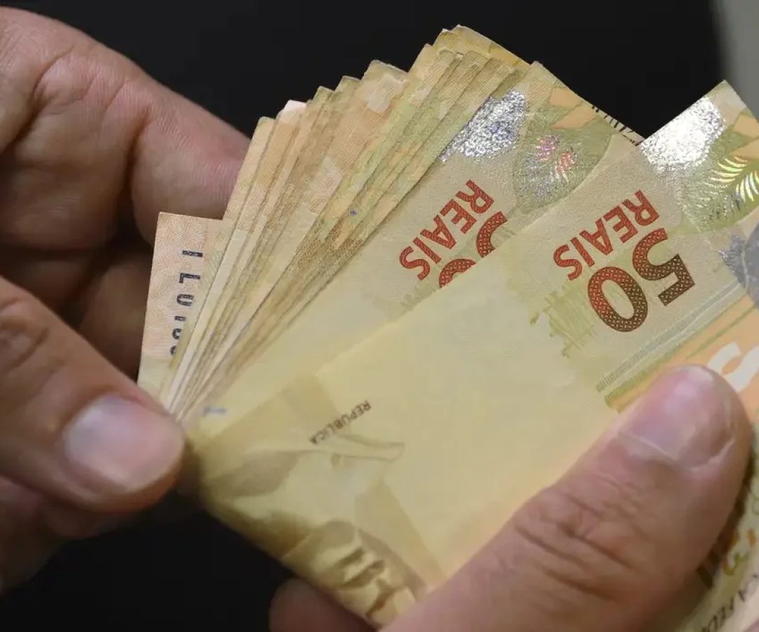 Fotografia para ilustrar matérias sobre empréstimos. Empilhamento de cédulas de real e moedas brasileiras ao lado de um capacete de proteção da construção civil e gráficos de crescimento financeiro. Proventos em construção: Com projeção de dividend yield de até 10,4%, o segmento de habitação popular ganha a preferência de analistas para a geração de caixa em agosto. Carteiras recomendadas: Com até 10,4% em dividendos Empiricus substitui Cyrela por Direcional